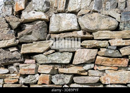 A wall made of different stones with grey, orange and brown colours. Stock Photo