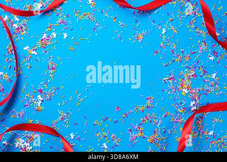 Red ribbon and multi colored confetti on a blue background. Happy New Year and Christmas designs. With space for text. Stock Photo