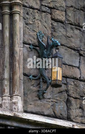 A close-up of a bronze street lamp in the shape of a mystical dragon on a stone wall, holding a lantern in its mouth. High resolution photo. Stock Photo