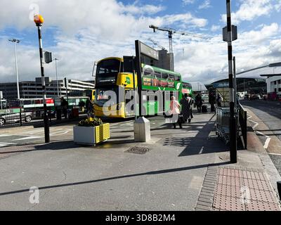 Dublin, Ireland - October 21, 2025: Bright day at a Dublin bus terminal with a green double decker bus and pedestrians. Stock Photo