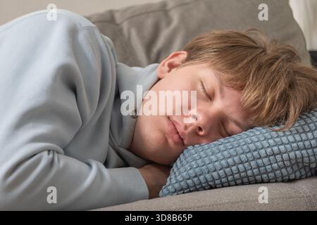 Young caucasian man sleeping peacefully on sofa at home, resting with eyes closed on soft pillow in calm comfortable living room environment. Autumn d Stock Photo