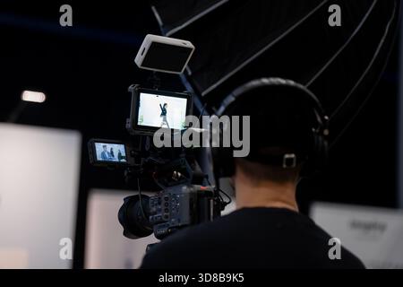Professional videographer recording a presenter on a broadcast camera equipped with external displays and softbox lighting in a modern studio environm Stock Photo