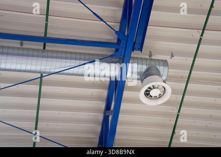Exposed ventilation ductwork and ceiling-mounted air outlet installed on blue steel support beams, showing HVAC infrastructure in industrial interior Stock Photo