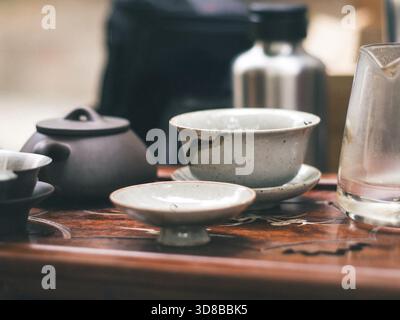Close-up of rustic traditional gongfu ceramic tea bowls and a dark clay teapot arranged on an ornate wooden tray, evoking a calm, traditional tea cere Stock Photo