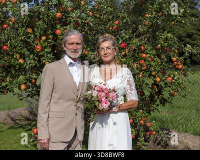 Elderly couple's wedding, look in front of a tree with lots of red apples Stock Photo