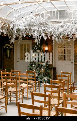 Chairs are arranged neatly in an indoor venue adorned with a Christmas tree and festive decorations. Stock Photo
