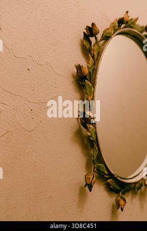 A round mirror adorned with dried flowers hangs on a textured wall, adding charm to the cozy room ambiance. Stock Photo