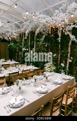 Tables are beautifully arranged with flowers and candles in a cozy garden area perfect for a special event. Stock Photo