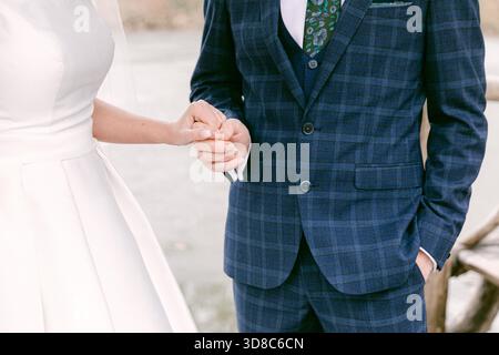 A man and woman stand close, holding hands, dressed in elegant outfits, enjoying a serene moment by the water. Stock Photo