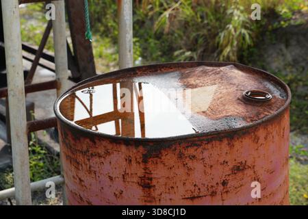 Weathered metal barrel with collected rainwater reflects its surroundings, showcasing the rustic texture and industrial decay. Perfect for themes of Stock Photo