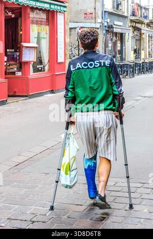 Young man with broken leg in plaster cast using medical forearm crutches as walking aid in city center - Tours, Indre-et-Loire (37), France. Stock Photo