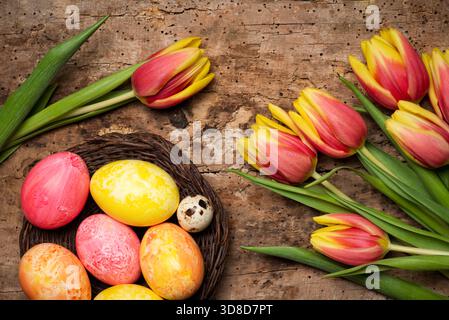 Colorful red and yellow tulips with hand painted Easter eggs on a wooden table tabletop view with copy space Stock Photo