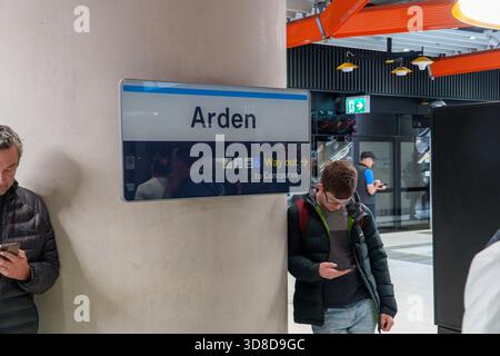 Melbourne, VIC, Australia. November 30, 2025. - Passengers interact with their phones beside a prominent Arden Station sign, showcasing the modern Met Stock Photo