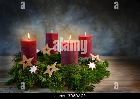 Four red candles on an Advent wreath, two are lit for the second advent, small stars and cinnamon cookies as Christmas decoration, bluish background, Stock Photo