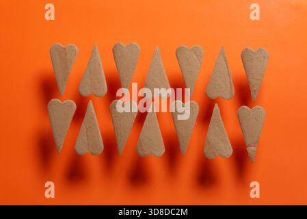 This image features heart-shaped sand forms arranged symmetrically on a vibrant orange background, creating a visually appealing abstract composition. Stock Photo