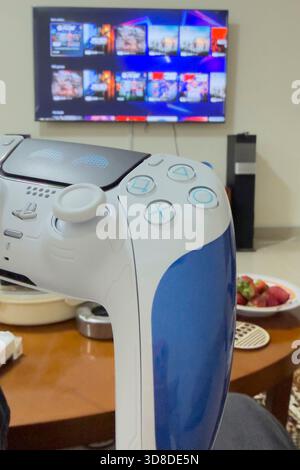 Doha, Qatar - November 28, 2025: A gamer is playing Play Station 5 at home, his hand holding Dual sense joystick which is the new wireless controller. Stock Photo
