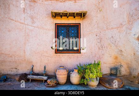 Traditional Moroccan window with ornate ironwork pottery and plants on pink adobe wall Stock Photo