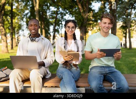 Students Work Together in a Park Using Laptops and Tablets During a Sunny Afternoon Stock Photo