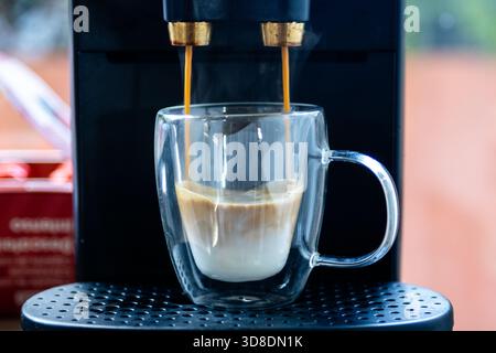 Fresh espresso brewing from an automatic coffee machine into a double walled glass cup, creating a morning beverage Stock Photo