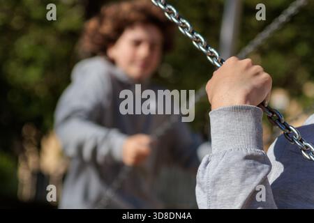 Child's hand gripping a metal chain on a swing set at an outdoor park, expressing childhood fun and recreation Stock Photo