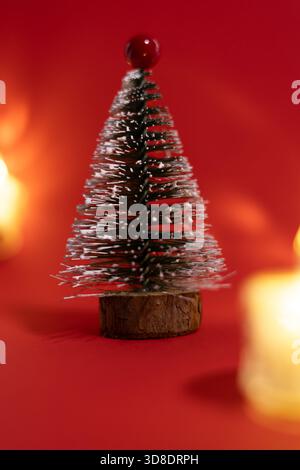 A small decorative Christmas tree with a wooden base, covered in white glitter, standing on a bright red background. Stock Photo