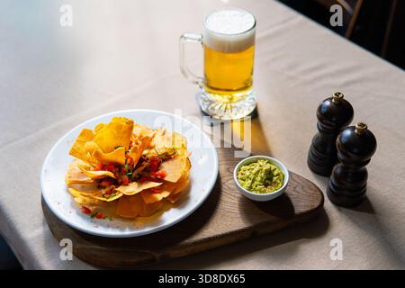Nachos or tortilla chips with fresh guacamole, mug of beer, and shakers on a table. Stock Photo