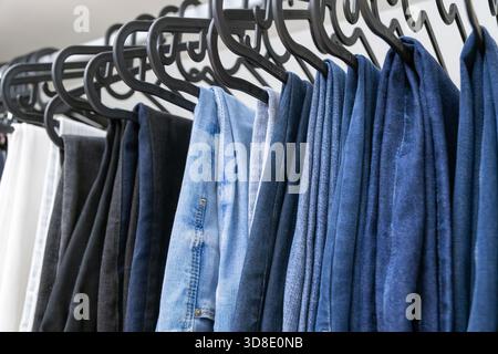 Multiple pairs of folded denim jeans hanging on black hooks in a tidy organized wardrobe with soft neutral lighting Stock Photo