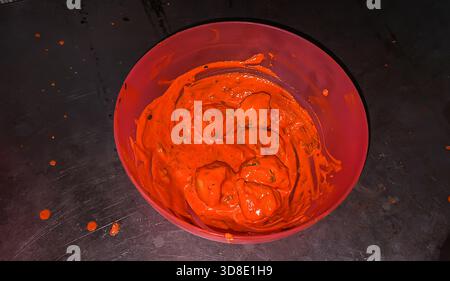 marinated momos coated in bright red spicy sauce inside plastic mixing bowl Stock Photo