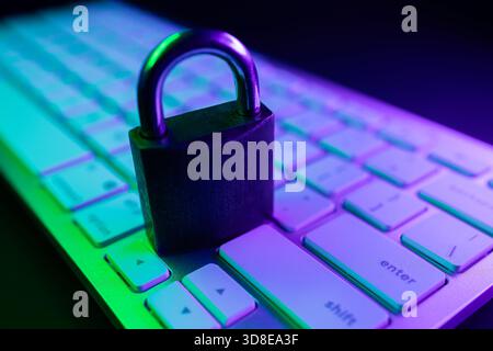 A padlock rests on a computer keyboard illuminated by vibrant purple and green lights. This scene symbolizes the importance of cyber security and prot Stock Photo
