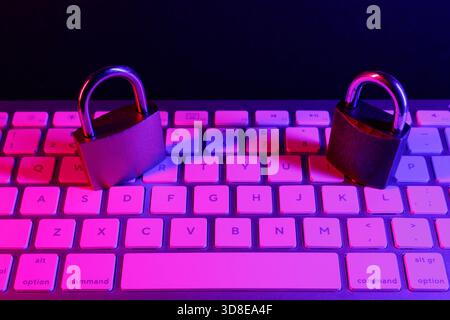 Two padlocks rest on a computer keyboard, symbolizing the need for internet security. The setting is dark with purple lighting, emphasizing the signif Stock Photo