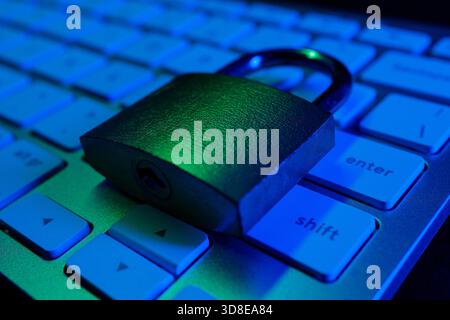 A padlock rests on a computer keyboard, illuminated by blue light, representing the importance of cyber security. This scene highlights the need for o Stock Photo