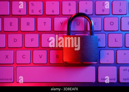 A lock rests on a keyboard illuminated by vibrant purple and pink lights. This scene symbolizes the importance of cybersecurity in protecting online i Stock Photo