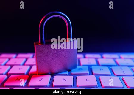 A metal padlock sits on a keyboard, representing cyber security measures. The scene is illuminated with colorful lights, emphasizing the importance of Stock Photo