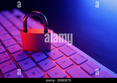 A padlock rests on a computer keyboard, representing the importance of cyber security and internet safety. The ambient lighting enhances the tech-focu Stock Photo