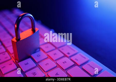 A metal padlock rests on a keyboard, representing the importance of cyber security and internet safety. The ambient lighting adds a futuristic touch t Stock Photo