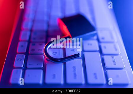 A padlock is placed on a computer keyboard, symbolizing the importance of cyber security. The scene is illuminated with blue and red lighting, emphasi Stock Photo