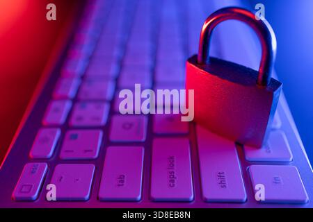 A padlock is placed on a computer keyboard, symbolizing cyber security. The scene is enhanced with vibrant, colorful lighting, emphasizing the importa Stock Photo