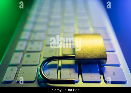 A secure padlock rests on a computer keyboard, representing the importance of cyber security and protecting personal data online. The setting is illum Stock Photo
