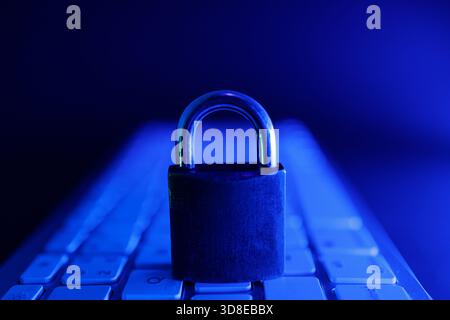 A padlock sits securely on a keyboard, surrounded by a blue glow. This scene highlights the critical role of cyber security in protecting online data Stock Photo