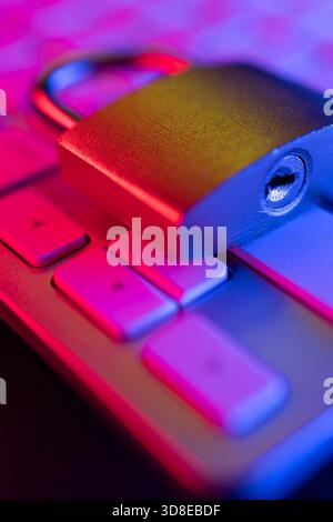 A combination lock sits on a computer keyboard illuminated in colorful lighting. This scene highlights the importance of cyber security in protecting Stock Photo