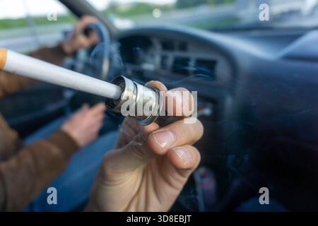 A cigarette is lit with the cigarette lighter in the car. Smoke is in the air. white and brown cigarett. lighter Stock Photo