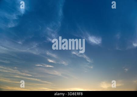 Deep Blue Sky with Wispy Clouds and Warm Evening Glow Stock Photo
