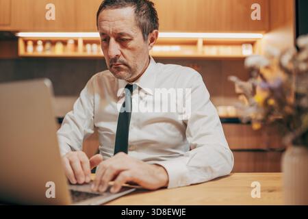 Professional man in formal attire using a laptop in a home office environment, concentrating on work. Selective focus. Stock Photo