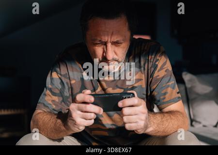 Close-up of a middle-aged man studying his phone with a tense, concentrated look, lit by strong natural light. Selective focus. Stock Photo