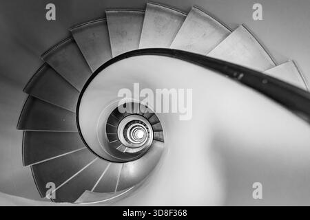 Overhead view of a grey spiral staircase in Geneva, Switzerland. The black and white architectural image shows a descending circular flight of steps. Stock Photo