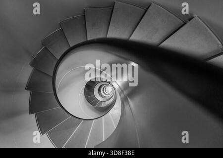 Overhead view of a grey spiral staircase in Geneva, Switzerland. The black and white architectural image shows a descending circular flight of steps. Stock Photo