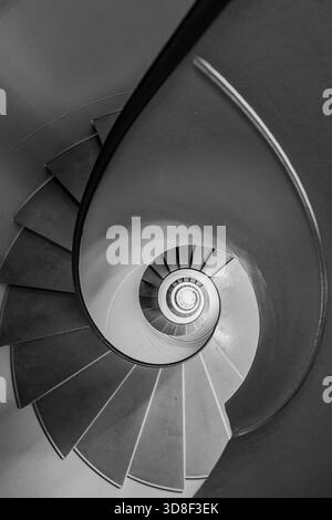 Overhead view of a grey spiral staircase in Geneva, Switzerland. The black and white architectural image shows a descending circular flight of steps. Stock Photo