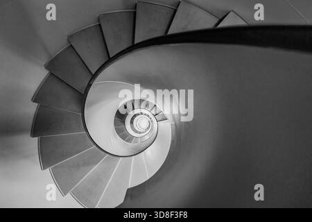 Overhead view of a grey spiral staircase in Geneva, Switzerland. The black and white architectural image shows a descending circular flight of steps. Stock Photo