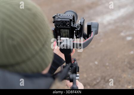 Professional filming setup with a mirrorless camera on a gimbal stabilizer held by an operator capturing stabilized shots in cold outdoor conditions Stock Photo