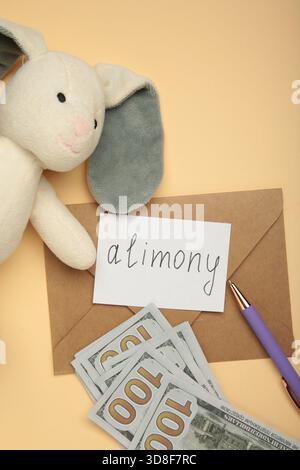 Toy bunny and envelope with word Alimony and money on beige background. Top view Stock Photo
